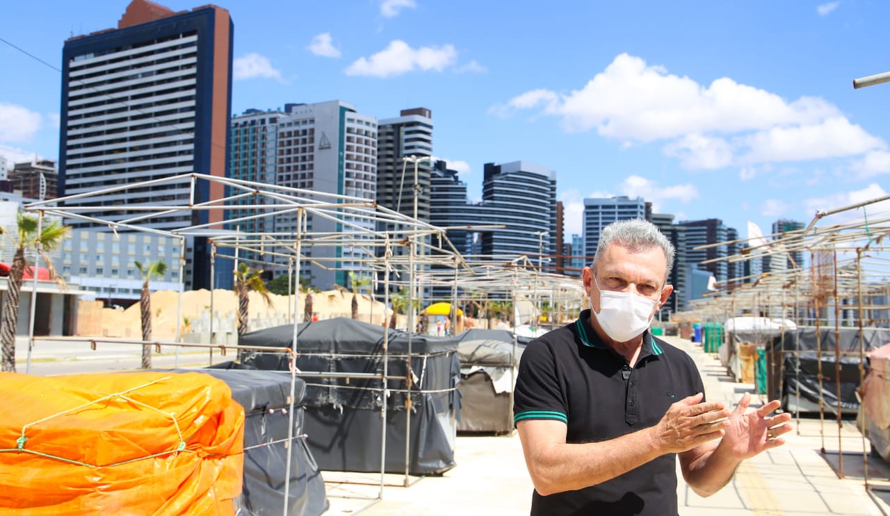 sarto fala olhando para uma câmera de vídeo na frente dos boxes da feira de artesanato da beira-mar